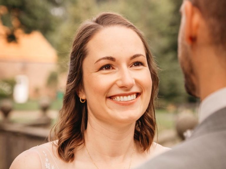 Lächelnde Frau in Hochzeitskleid, schaut glücklich einem Mann entgegen. Geschminkt von ALMA Kosmetik & Wellness