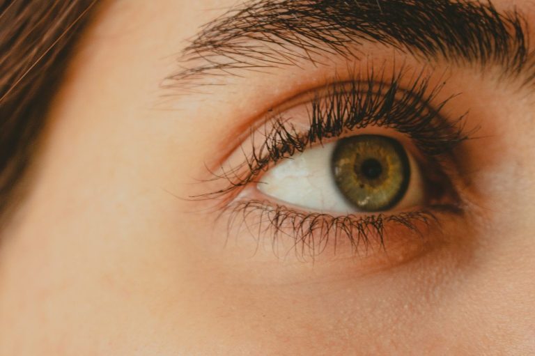 Nahaufnahme eines menschlichen Auges mit grünem Iriskreis und langen Wimpern.